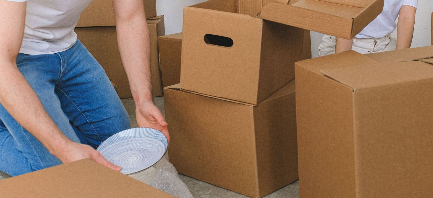 Serious young relocating man and woman in casual outfits packing fragile things into carton boxes while preparing for moving into new apartment in daylight