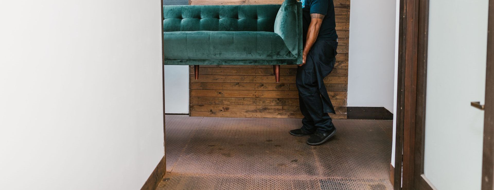 A mover carries a green sofa indoors, showcasing modern interior design and relocation services.