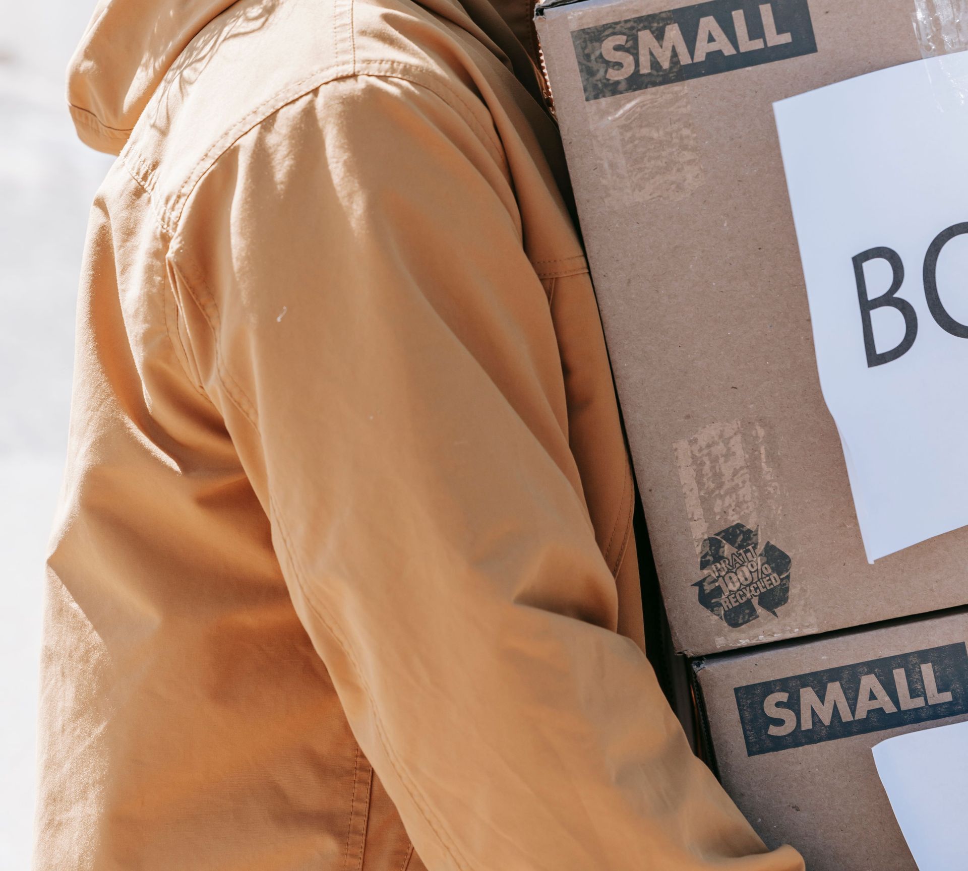 Couple carrying boxes outdoors, moving to a new home. Bright daylight scene.