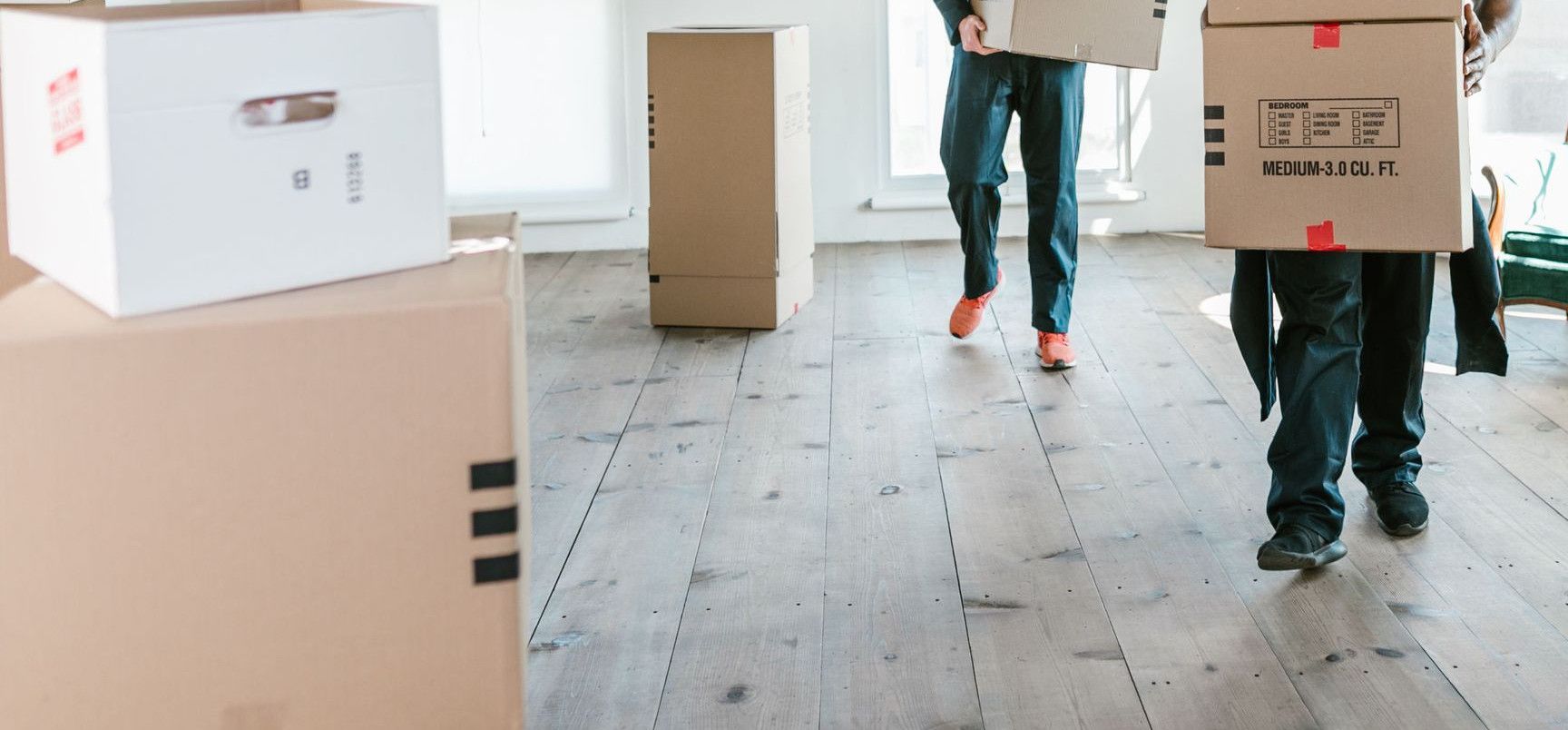 Two movers carrying boxes in a sunlit room, ready to assist with relocation.
