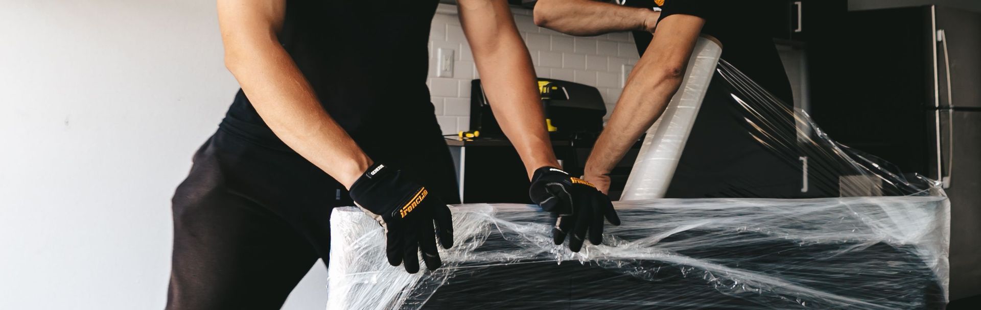 Two masked men moving a securely wrapped item in a modern room.