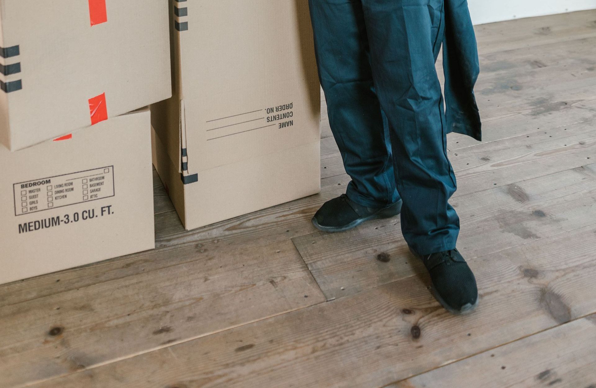 Smiling delivery worker in uniform standing with packaged boxes indoors.